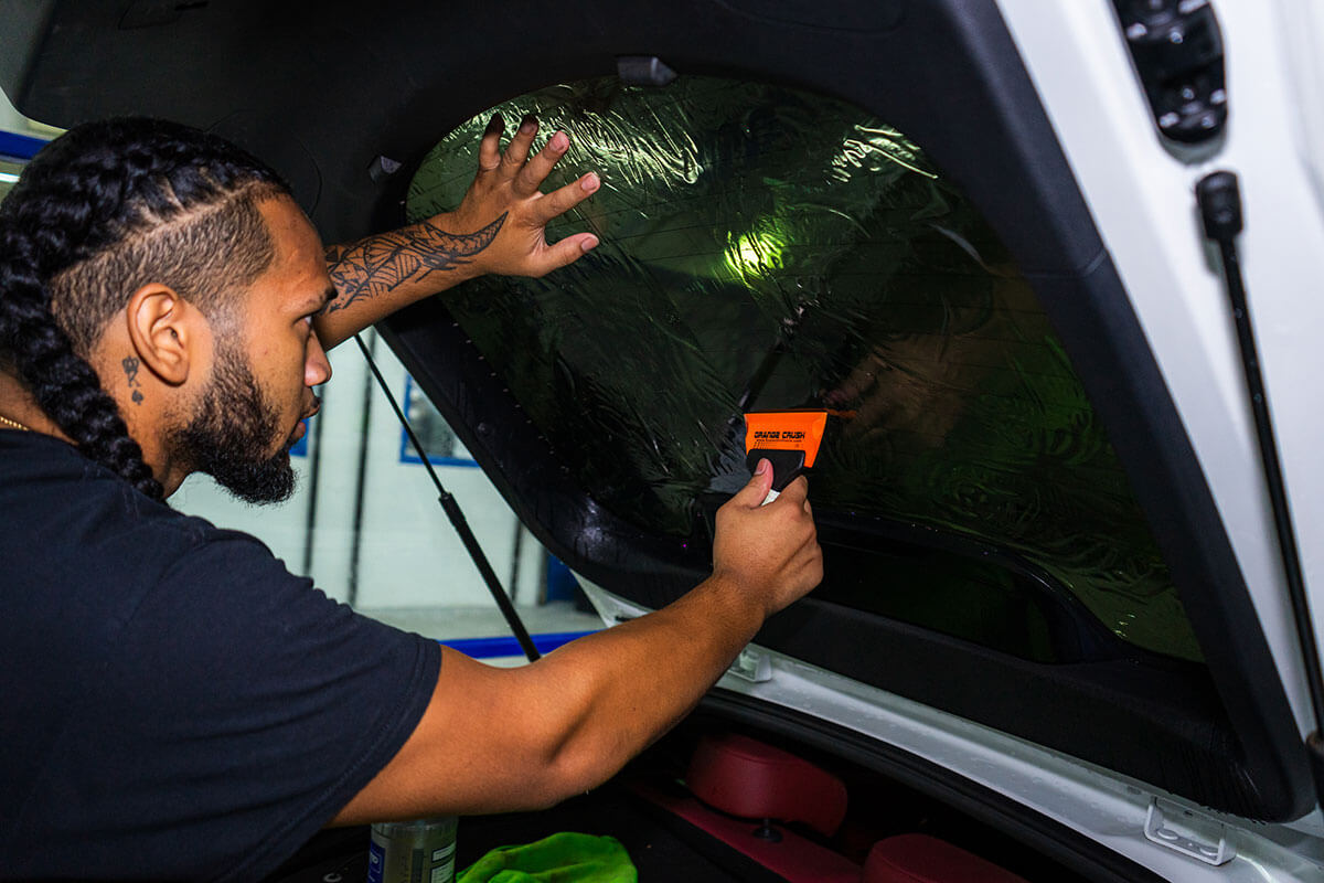 Installer squeegeeing window film onto the inside of a vehicle's rear hatch glass